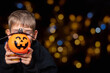 © Alena - A child holding an orange pumpkin-shaped basket with a grinning face and a bat on a black background with bokeh