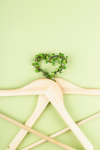 Conscious Consumption Slow Fashion Concept. Heart Of Clothes Hangers Entwined With Plant On Green Background. Sustainable Eco Lifestyle. Top View Flat Lay