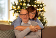 © Syda Productions - winter holidays and people concept - happy smiling senior couple hugging on sofa at home in evening over christmas tree lights on background
