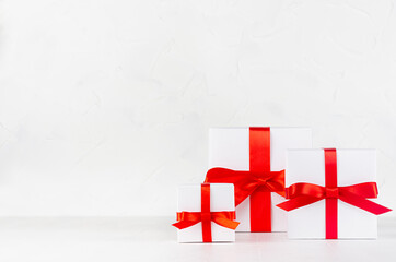 Wall Mural - Three festive white paper boxes for gift with red silk ribbon and bow  in white interior of elegant minimal style, copy space.