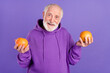 Portrait of attractive cheerful grey-haired man holding in hands two grapefruits isolated over bright violet purple color background