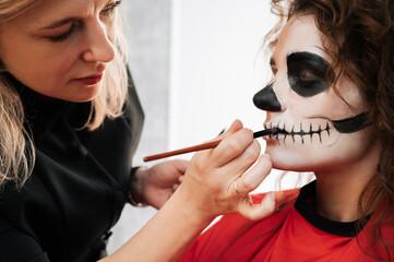 Wall Mural - A makeup artist makes up a demon to a young girl in a beauty salon. Halloween Celebration Concept