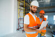 © fotofabrika - Two specialists supervisors in hardhats using laptop at construction site for work
