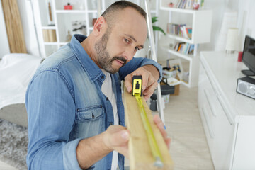 man measuring length of wood in his living room