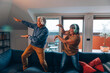 happy active senior couple plays and dances on sofa at home with headphones listening to music