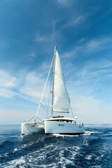 Luxury catamaran sailing under white sails on the blue azure sea on a sunny summer day. Travel, yachting, regattas concept