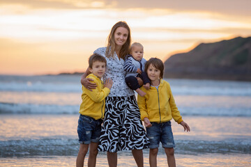 Canvas Print - Young mother with her beautiful children, enjoying the sunset over the ocean on a low tide in Devon