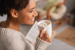 © LIGHTFIELD STUDIOS - Side view of happy african american woman holding cup of cocoa with marshmallows and blurred book at home