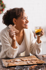 Canvas Print - African american woman holding homemade christmas gingerbread and tea in kitchen