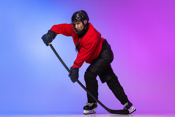 Full-length portrait of professional female hockey player training, dribbling puck isolated over gradient blue purple background.