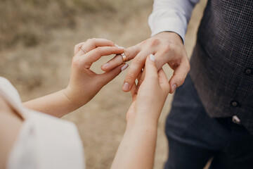 At the wedding ceremony, the bride puts the wedding ring on the groom's finger. Hands of newlyweds with rings close-up. Heterosexual young couple in love enjoying their wedding