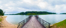 Panorama View Of Wooden Pier With Lifebuoy Over The Lake Near The Forest.