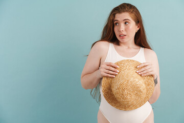 Wall Mural - Young ginger woman looking aside while posing with straw hat