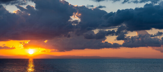 Wall Mural - Stunning dramatic, cloudy sunrise with a bright sun rising over a calm water. Natural background, Sardinia, Italy.