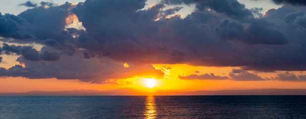 Wall Mural - Stunning dramatic, cloudy sunrise with a bright sun rising over a calm water. Natural background, Sardinia, Italy.