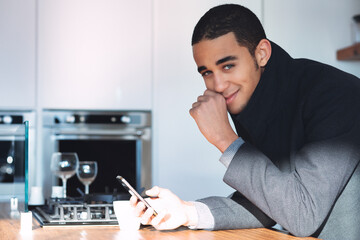 Amused young man smiling as he leans on a kitchen table