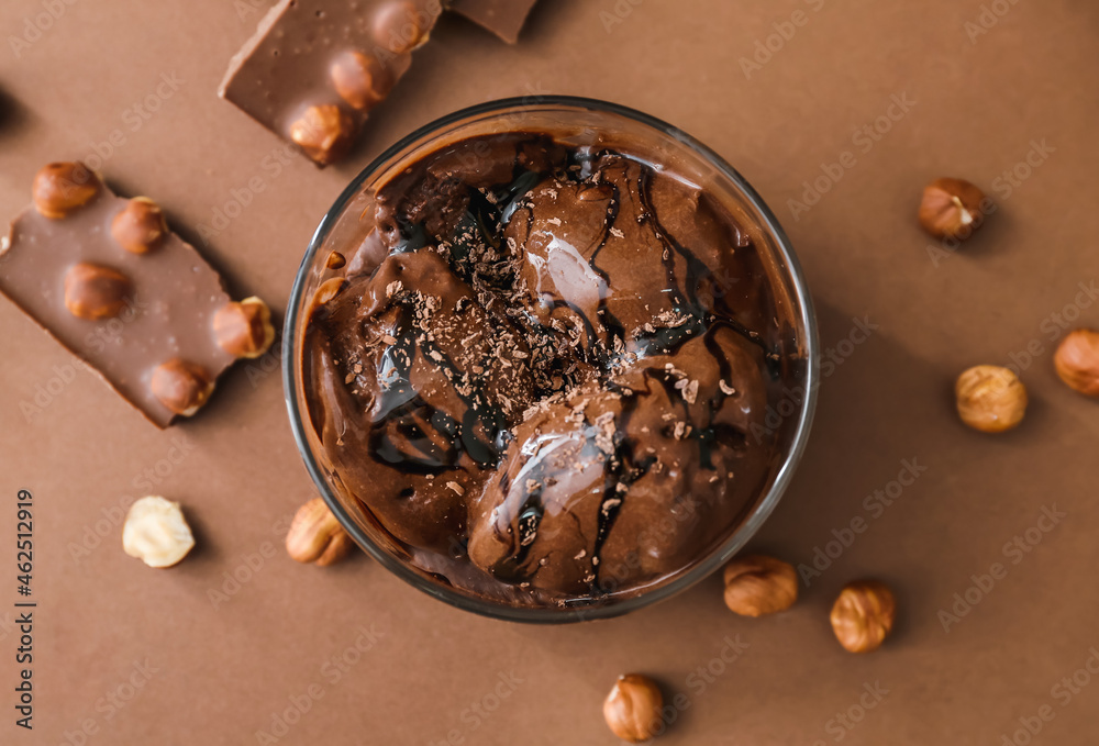 Bowl with delicious chocolate ice cream and hazelnuts on color background