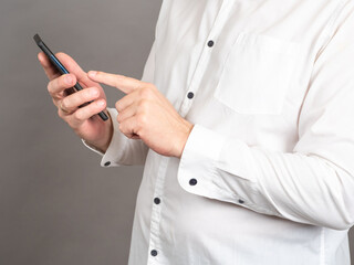 Poster - Men hands with smartphone. Unrecognizable person using mobile phone. Businessman using gadget. Man in white shirt looks at the information in his smartphone. Communication using electronic devices.
