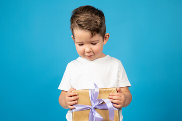 Wall Mural - Cute confused boy with a gift in his hands over blue background