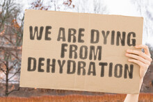 The Phrase " We Are Dying From Dehydration " On A Banner In Men's Hand With Blurred Background. Destruction. Die. Dramatic. Ecosystem. Exhaustion. Healthcare
