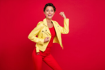 Poster - Photo of charming lucky young lady wear yellow jacket smiling rising fists isolated red color background