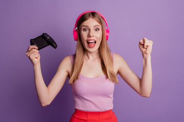 Portrait of cheerful astonished champion lady hold joystick open mouth wear headphones pink top on purple background