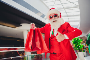 Sticker - Photo of confident pretty santa claus wear dark glasses holding bargains showing thumb up indoors shopping center