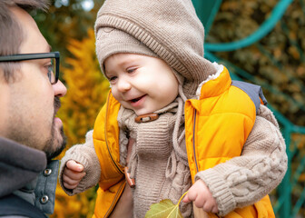 Cute one-year-old child looking at his father and smiling. A young father holds his one-year-old son in his arms