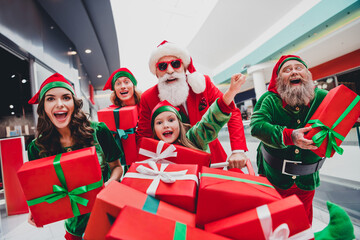 Poster - Photo of excited lucky santa claus assistants wear costumes smiling rising fist buying many gift packages indoors shopping center