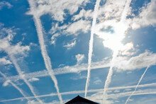 Contrails Over Residential Area With Sun Behind Clouds