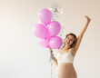 Portrait of beautiful Happy pregnant woman holding balloons, looking at camera and smiling on gray background. Pregnant woman with colorful balloons. Beauty girl. It's a boy.