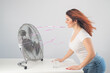 © Михаил Решетников - A red-haired Caucasian woman chills by the electric fan and drinks a cold drink. Climate control in the apartment