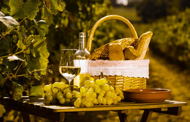 Wall Mural - still life with glass of white wine grapes and picnic basket on table in field