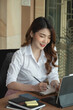 © Natee Meepian - Portrait charming asian woman taking note on notepad while video conference via digital tablet