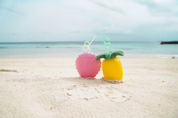 Exotic tropical summer drinks in pink shell shaped and pineapple shaped  bottle on the sandy beach background, Maldives