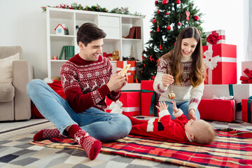 Wall Mural - Photo of nice parents play little infant father hold telephone take selfie wear sweater in decorated x-mas home indoors