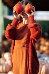 Wall Mural - Portrait of happy woman with ripe orange pumpkins in hands close eyes near wagon with orange pumpkin on farmers market in brown sweater, dress. Cozy autumn vibes Halloween, Thanksgiving day