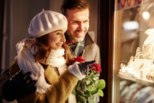 Smiling Couple Looking In Shop Window Of Jewellery Store At Christmas Time