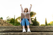 © VITTA GALLERY/Westend61 - Young redheaded woman using laptop and cheering, sitting on steps in a park