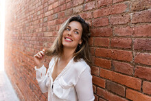 Portrait Of Smiling Woman Leaning On Brick Wall