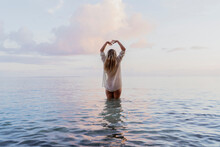 Rear View Of Young Woman Wearing White Blouse Inside Sea During Sunset