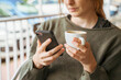 © VITTA GALLERY/Westend61 - Close-up of young woman using cell phone and holding coffee cup