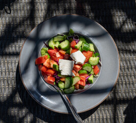 Wall Mural - Summer healthy food served outdoor in sunlights, vegetable greek salad made with fresh cucumber, tomatoes, onion, feta cheese