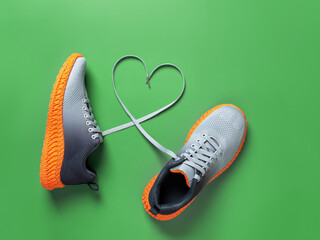 shoelace heart symbol between gray textile sneakers with grooved orange sole on grassy green backgro