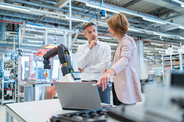 Businessman and businesswoman with laptop talking in a modern factory hall