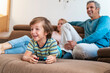 © Daniel Ingold/Westend61 - Boy lying on couch at home playing video game with parents watching