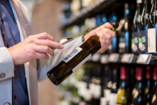 Mature Man Choosing Wine In Supermarket, Scanning Product Information Ith His Smartphone