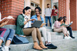 © Drazen - Happy multi-ethnic female students have fun while using laptop in front of university building.