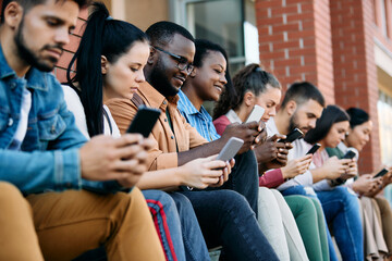 Wall Mural - Multi-ethnic group of students use cell phones while relaxing outdoors.