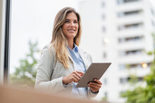 Portrait Of Young Businesswoman Using Tablet, Office Buildings In The Background